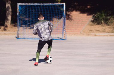 Beton bir futbol sahasında futbol oynayan tanınmamış bir sporcunun arka görünüşü boş bir amaç, sağlıklı yaşam tarzı ve kentsel spor kavramı, metin için yer kopyalama