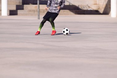 Tanınmayan bir futbolcunun ayakları beton bir sahada top oynuyor, şehirde sağlıklı yaşam tarzı ve şehir sporu kavramı, metin için yer kopyalama