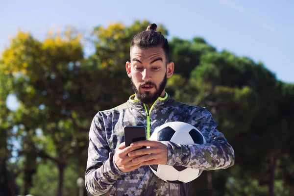 Модний Спортсмен Футбольним Ячем Консультує Свій Мобільний Телефон Здивованим Виразом — стокове фото