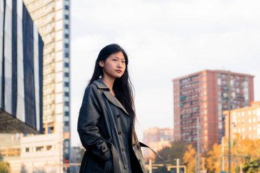 Trençkotlu genç Asyalı kadın şehrin önünden geçiyor, şehir yaşam tarzı konsepti, metin için kopyalama alanı