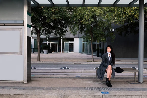 Tramvay durağında Asyalı bir kadın oturuyor ve treni bekliyor, toplu taşıma konsepti ve şehir yaşam tarzı.