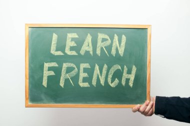 Elinde tebeşirle yazılmış LEARN FRENCH mesajı olan bir yazı tahtası var.