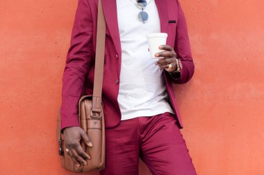 Takım elbiseli, elinde çantasıyla kırmızı arka planda kahve tutan tanınmamış bir Afrikalı işadamı.