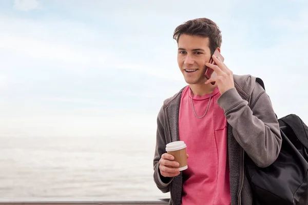 happy young man with a coffee talking by mobile phone outdoors, concept of technology of communication and urban lifestyle, copy space for text