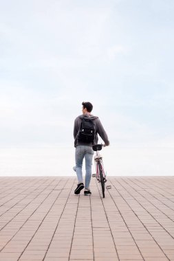 Bisiklet sürerken genç bir adamın arkadan görünüşü, ekolojik ve sürdürülebilir ulaşım kavramı, metin için kopya alanı, dikey fotoğraf