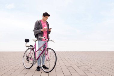 Cep telefonuna bakarken elinde kahve tutan bisikletli genç adam, iletişim konsepti ve sürdürülebilir şehir ulaşımı, metin için kopyalama alanı