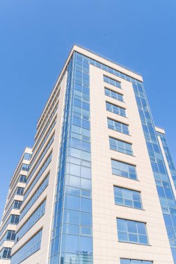 Aydınlık bir yaz gününde açık mavi gökyüzüne karşı modern bir ofis binası.