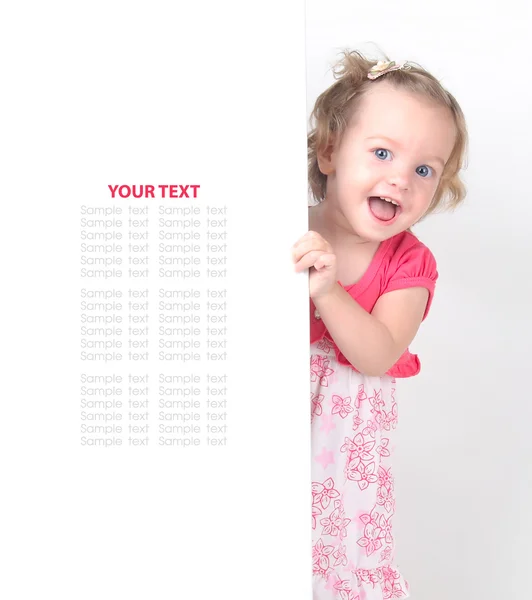 Happy little girl peeking out from behind a white advertisement board — Stock Photo, Image