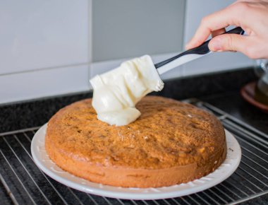 Tanınmayan el, spatulayla havuçlu kekin üzerine peynir ve şeker serpiyor.