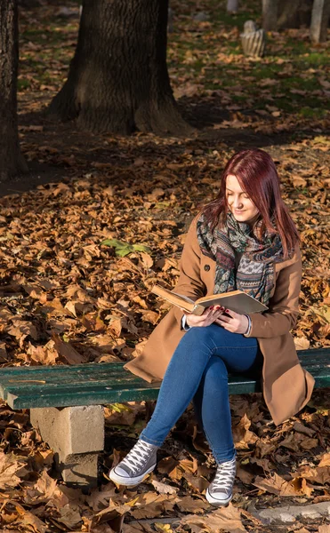 Rödhårig tjej sitter på bänken i park — Stockfoto
