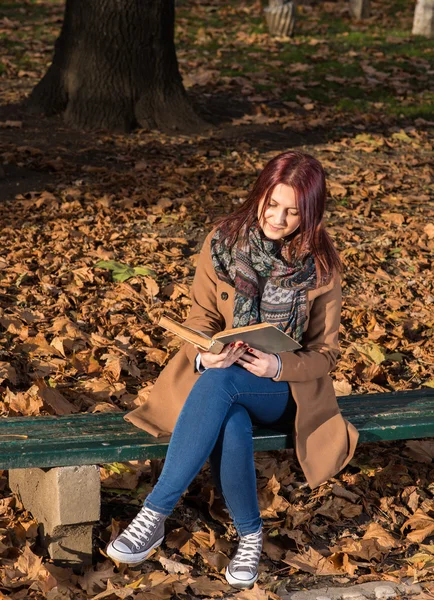 Rödhårig tjej sitter på bänken i park — Stockfoto