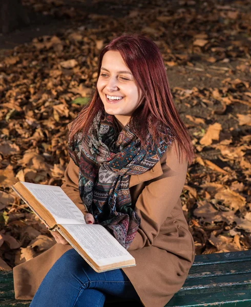 Redhead girl sitting on bench in park and reading book — Stock Photo, Image