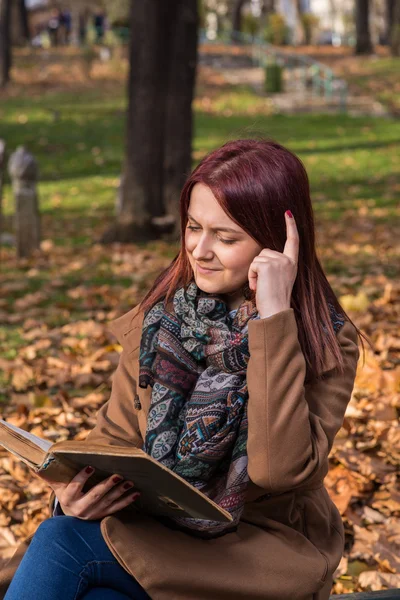 Rödhårig tjej sitter på bänken i park och läsa bok — Stockfoto