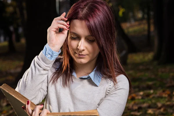 University girl sitting in park and reading a book — Stock Photo, Image