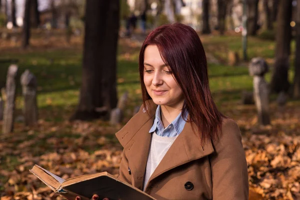 Redhead girl sitting on bench in park and reading book — Stock Photo, Image