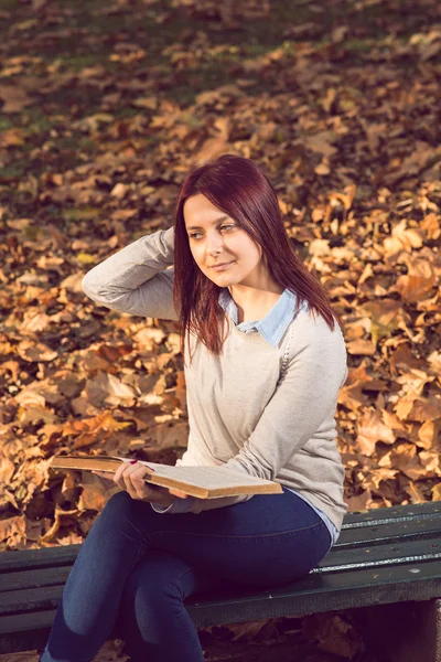 Flickan sitter på bänken i ark och läsa en bok — Stockfoto