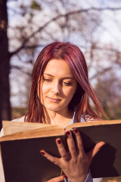Flickan sitter på bänken i ark och läsa en bok — Stockfoto