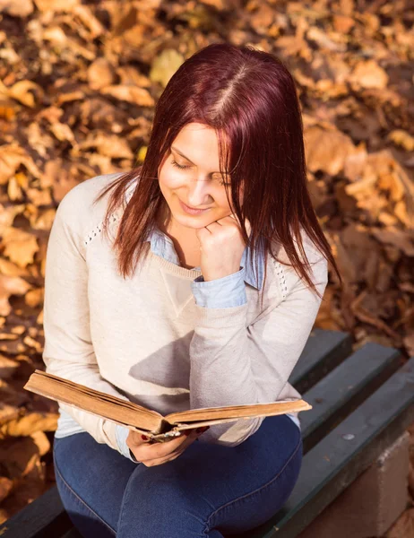 Flickan sitter på bänken i ark och läsa en bok — Stockfoto