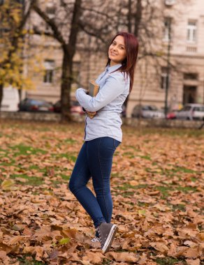 Kızıl saçlı kız ayakta ve bir kitap park holding