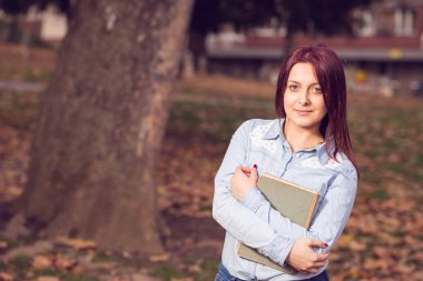 Kızıl saçlı kız ayakta ve bir kitap park holding