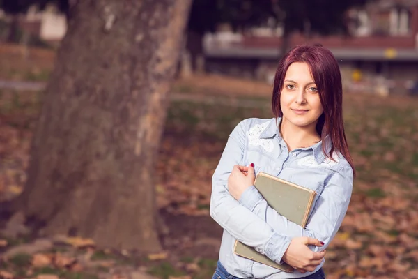 Rödhårig tjej står och håller en bok i parken — Stockfoto