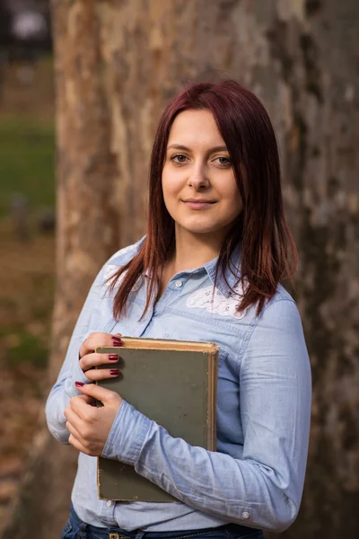 Rödhårig student tjej håller en bok i parken — Stockfoto