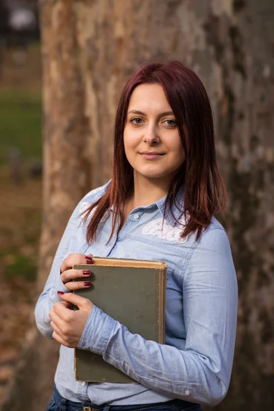 Ruiva estudante menina segurando um livro no parque — Fotografia de Stock