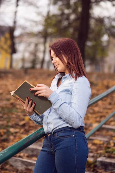 Estudante ruiva menina lendo um livro no parque — Fotografia de Stock