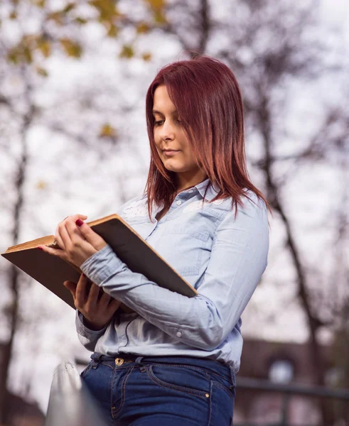 Rödhårig student tjej läser en bok i parken — Stockfoto