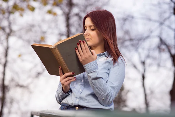 Rödhårig student tjej läser en bok i parken — Stockfoto