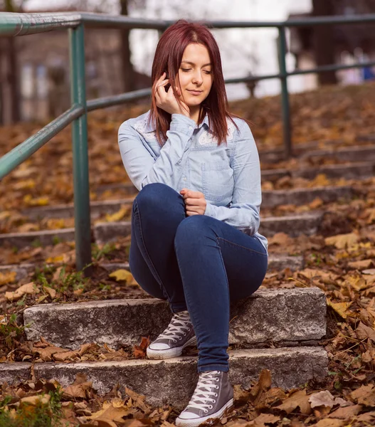 Redhead girl sitting on stairs and typing on phone — Stock Photo, Image