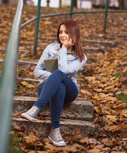 Redhead girl sitting on stairs and holding a book — Stock Photo, Image