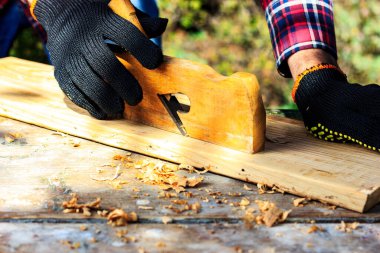 Arka bahçede bir adam uçakla ahşap kalaslarda çalışıyor. ÇEVİR