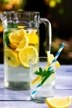 Bir bardak limonata ve pipet. Arka planda, bir sürahi dolusu limon ve limon..