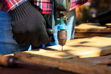 Adam ahşap bir tahtayı el matkabıyla deliyor.