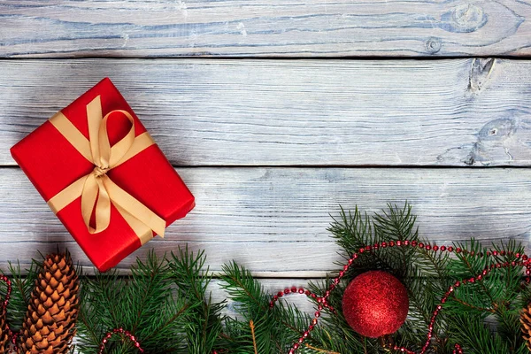 Cadre de Noël avec un cadeau de Noël rouge et branches de sapin sur un fond en bois blanc clair. Vue d'en haut. — Photo