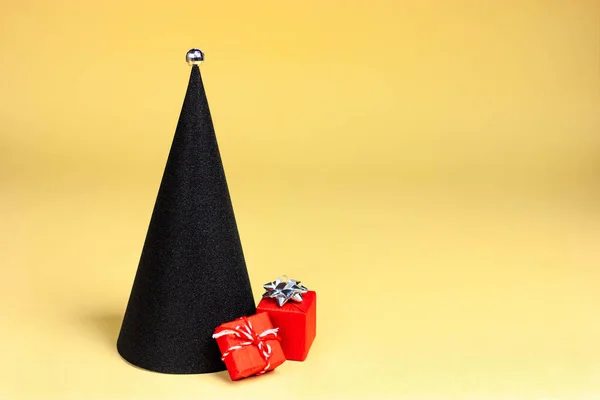 Sarı zemin üzerinde kırmızı hediyeler olan siyah minimalist bir Noel ağacı. pop-art tarzı — Stok fotoğraf