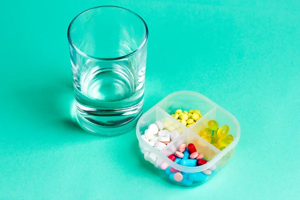 Um copo de água e comprimidos médicos numa caixa. Pillbox com pílulas multicoloridas — Fotografia de Stock