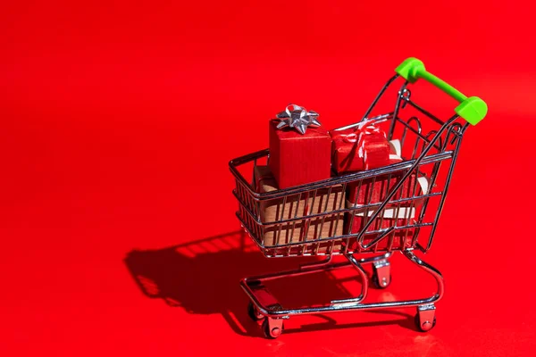 Carrinho de supermercado cheio de presentes de Natal em um fundo vermelho em estilo pop-art com sombra dura. Tema de presentes para o ano novo, Natal, sexta-feira preta. — Fotografia de Stock