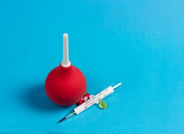 Mavi arka planda Enema, cıva termometre ve tıbbi haplar..