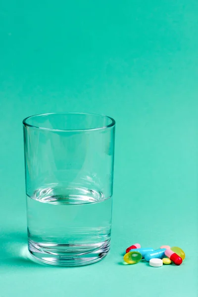 Píldoras farmacéuticas de color, vitaminas y un vaso de agua. — Foto de Stock