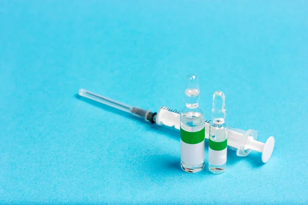 Spuit en drie ampullen op een blauwe achtergrond. Antigif in ampullen. Coronavirusvaccin. — Stockfoto