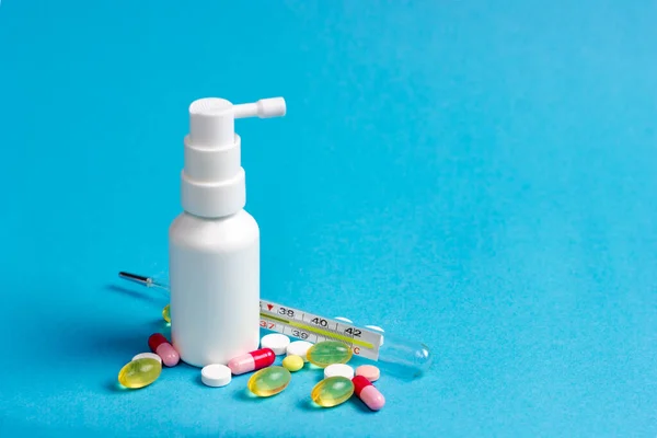 Compresse farmaceutiche, pillole e un termometro al mercurio con una bottiglia di spray alla gola su fondo blu. — Foto Stock