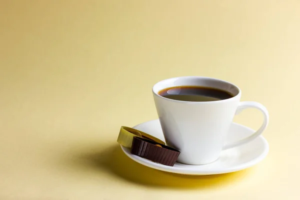 Белая чашка кофе и шоколад на желтом фоне — стоковое фото