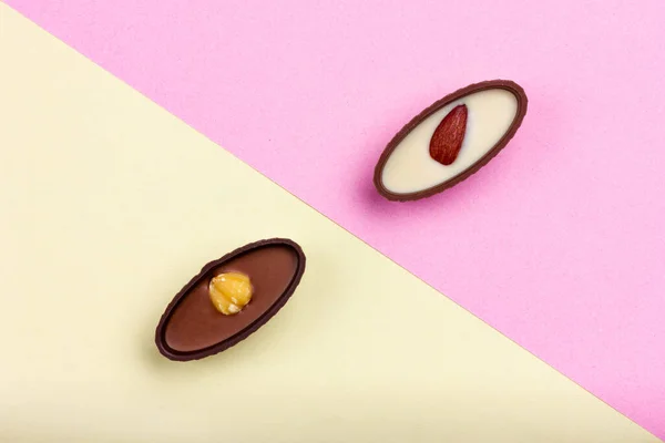 两个有坚果和彩色背景的巧克力糖果。诊断背景-黄色、粉色 — 图库照片