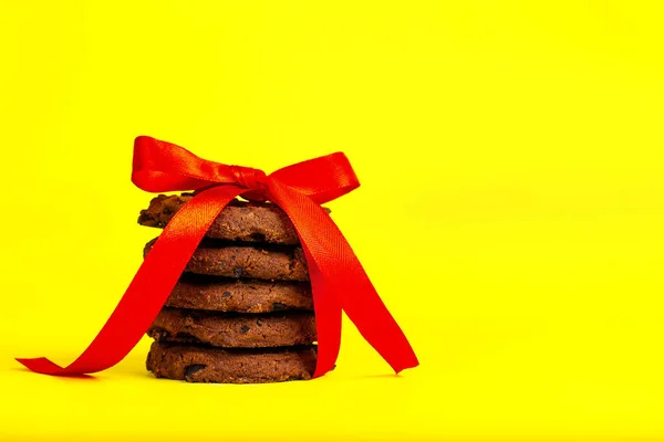 Biscoitos com chips de chocolate amarrados com uma fita vermelha em um fundo amarelo. — Fotografia de Stock