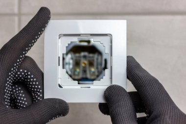 Eldivenli eller elektrik prizinin çerçevesini tutuyor. Çamaşırhanedeki elektrik prizi..