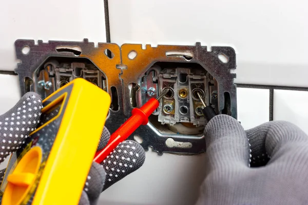 男は分解されたコンセントの電圧をマルチメーターでチェックします。 — ストック写真