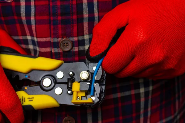 Ekose gömlekli ve kırmızı iş eldivenli bir adam sarı penseyle elektrik kablolarını söküyor..
