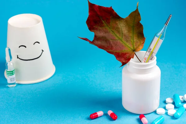 Medicamentos, un frasco blanco de medicinas, un termómetro de mercurio y la emoción de la felicidad sobre un fondo azul. El tema del tratamiento de los resfriados. — Foto de Stock